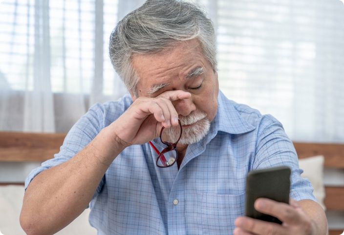 An old man is scratching his eyes while holding a phone